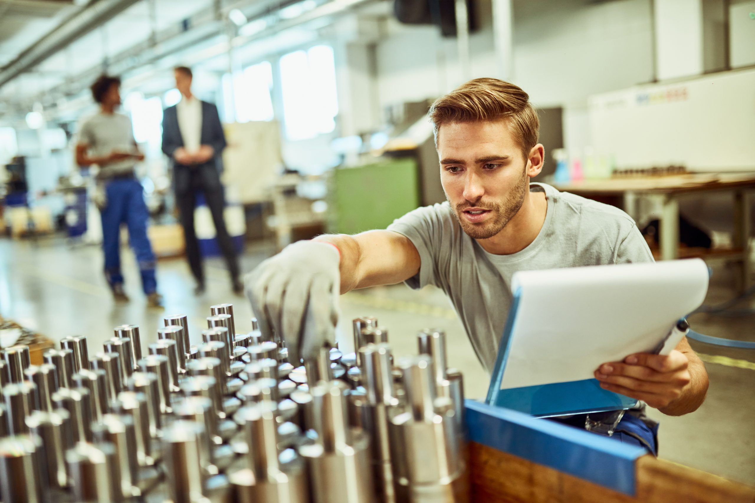 Young steel worker inspecting quality of finished machine parts in a factory.